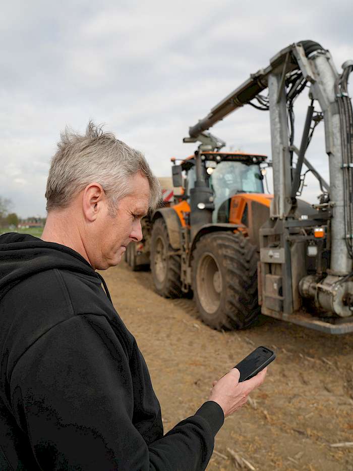Mann mit Handy vor Landmaschine